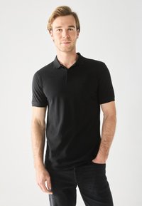 Sort polo-shirt lavet af glat bomuld, med en klassisk krave, korte ærmer og en tætsiddende design, kombineret med mørke jeans.