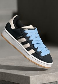 Black suede sneaker with light blue laces, white three-stripe design, and tan rubber sole. Features padded collar and textured upper.