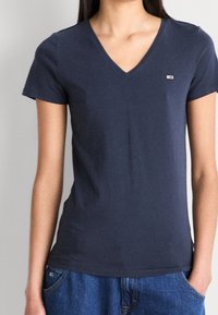 Granatowa koszulka z dekoltem w kształcie litery V, wykonana z miękkiej bawełny, z krótkimi rękawami i małym logo na piersi. Połączona z dżinsowymi szortami.