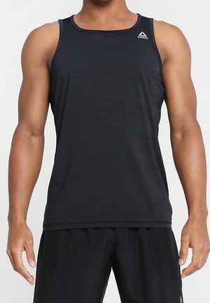 Mężczyzna w czarnym sportowym topie bez rękawów Reebok i czarnych szortach na jednolitym tle.