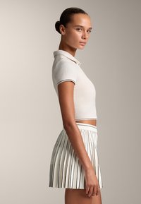 Crop top i ljusbeige med ribbad textur och korta ärmar, kombinerad med en vit kjol med veck och svarta ränder.