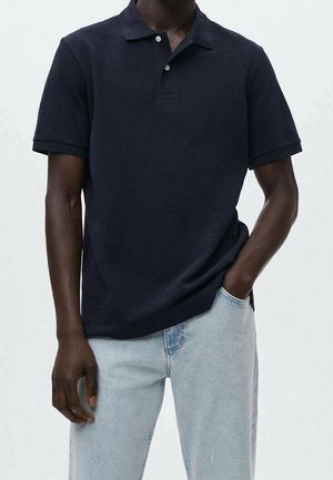 Polo bleu marine avec col côtelé, manches courtes et fermeture à deux boutons à l'avant. Porté avec un jean bleu clair. Texture lisse.