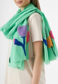 Groene sjaal met bloemenborduurwerk in paars, roze en blauw. Lichtgewicht stof met franje randen, gedrapeerd over de schouders.