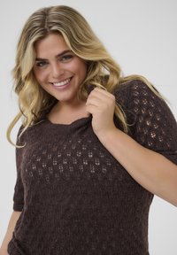 Brown knitted sweater with short sleeves and a scoop neckline, featuring a textured pattern and a loose fit. Fabric appears soft and comfortable.
