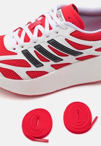 Piros hálós sportcipő fehér részletekkel, emelt talppal és fekete oldalsó mintázattal. Két piros fűzőt tartalmaz márkajelzéssel.