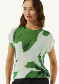 Groen en witte, korter mouw gebreide top met een groot bladerenpatroon. Zacht, licht materiaal met een ontspannen pasvorm en een ronde halslijn.