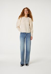 Romige gebloemde geborduurde trui met pofmouwen, gecombineerd met lichtblauwe, wijde jeans en zwarte schoenen met witte accenten.