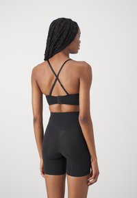 Black sports bra with crossover straps, paired with high-waisted black shorts. Both items made from smooth, stretchy fabric.