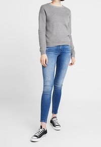 Gray sweater with round neckline, paired with blue skinny jeans featuring slight distressing, and black low-top sneakers with white soles.