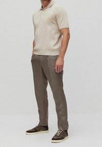 Beige short-sleeve polo shirt with ribbed texture, paired with light brown trousers and dark brown sneakers with white soles and laces.