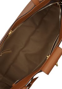 Interno di una borsa in pelle, foderato in tessuto beige, chiusura con zip, accessori in tonalità oro, presenta un comparto aperto e una tasca con zip.