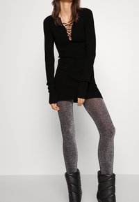 Svart långärmad stickad klänning med djup V-ringning och snörningsdetalj, matchad med glänsande svarta och silverprickiga leggings samt svarta ankelstövlar.