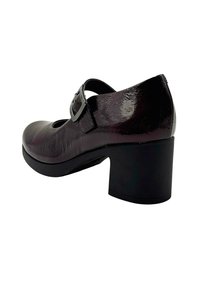 Zapato Mary Jane de charol negro con tacón medio grueso y correa de hebilla plateada, visto desde la parte trasera.