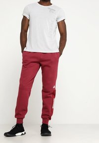 Ljusgrå t-shirt med kort ärm och tryck på framsidan, samt röda träningbyxor med tre vita ränder och logotyp. Svarta sportskor fulländar outfiten.