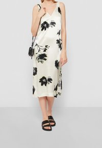 Krémové saténové šaty s květinovým vzorem v černé barvě, výstřih ve tvaru V a ramínka; doplněné černými klouzacími sandály.