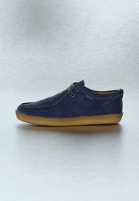Καθημερινό παπούτσι ναυτικού μπλε χρώματος με ταμπά λαστιχένια σόλα, φερμουάρ μπροστά, εμφανές ράψιμο και σχεδιασμό με χαμηλό προφίλ σε ουδέτερο φόντο.