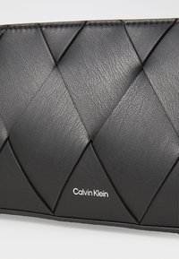 Svart plånbok i texturerad läder med ett vävt diamantmönster och subtila sömmar; har en vit Calvin Klein-logotyp.