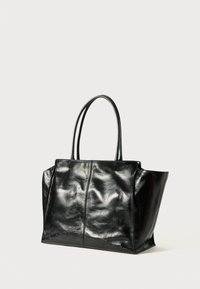 Fekete bőr táska sima textúrával, megnyúlt oldalakkal és két erős fogantyúval. Középen varrott, jellegzetes hardver nélkül.