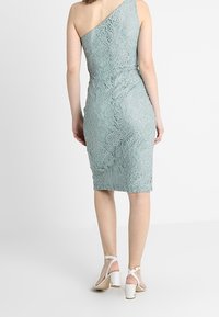 Enaxlad mintgrön spetsklänning, figursydd silhuett, blommönster, knälång, matchad med vita klackar med ankelsnörning.