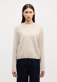 Lichtbeige gebreide trui met een ronde hals, lange mouwen en ribbelzoom. Geweven materiaal met een subtiel patroon. Donker denim broek.