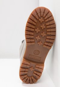 Timberlandin kengänpohja ruskeasta kumista, jossa on syvät urat pidon parantamiseksi, kohokuvioitu logo ja vahvistetut reunat kestävyys. 