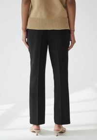 Zwarte rechtlijnige broek met een gladde textuur, gecombineerd met een ribbelige beige trui. Het uitzicht toont de achterkant en benadrukt de val van de stof.