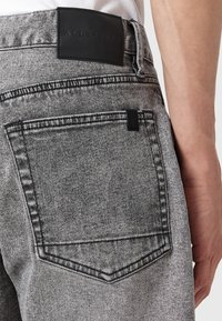 Svarta jeans i denim med en förblekt grå finish, med en läderlogo på midjebandet och en distinkt form på bakfickan.