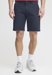 Navy blue cotton shorts with a flat front, side pockets, and rolled hems. Worn with white ankle socks and gray athletic shoes.