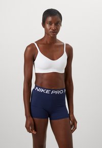 Vit sport-bh med tunna remmar; marinblå Nike Pro-shorts med vitt logo vid midjan. Slät, elastisk tyg, kroppsnära design.