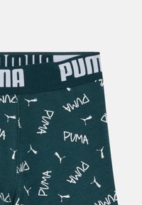 Donker groene Puma boxershorts met witte herhaalde Puma-logo's en silhouetten, en een zwarte tailleband met grote witte Puma-tekst.