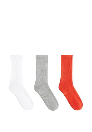 Trzy żeberkowane skarpety za kostkę w kolorach białym, szarym i czerwonym, ułożone obok siebie na białym tle.