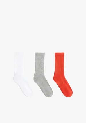 Drei gerippte Knöchelsocken in Weiß, Grau und Rot, nebeneinander auf einem weißen Hintergrund angeordnet.