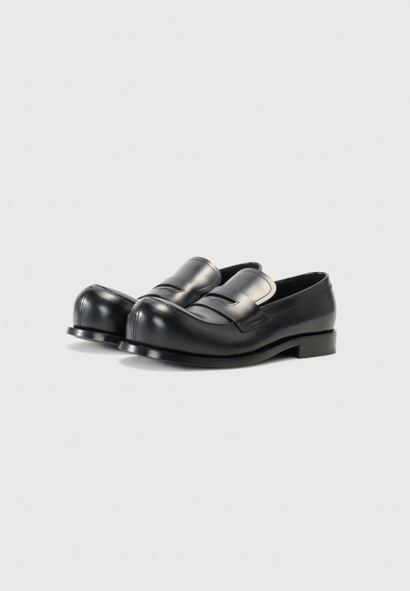 Schwarze Lederloafer mit abgerundeter Spitze, versehen mit einem dekorativen Riemen und minimalen Nähten. Glatte Oberfläche und ein niedriger, gestapelter Absatz.