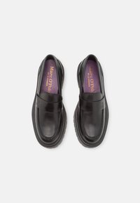Mocassins en cuir noir avec une texture lisse, bout rond et coutures surélevées. Dispose d'une large sangle sur le cou-de-pied et d'une semelle intérieure violette.