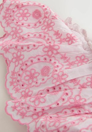 Lyserød blomsterbroderi med bølgede kanter på hvidt stof, der viser detaljeret syning og hulmønstre.