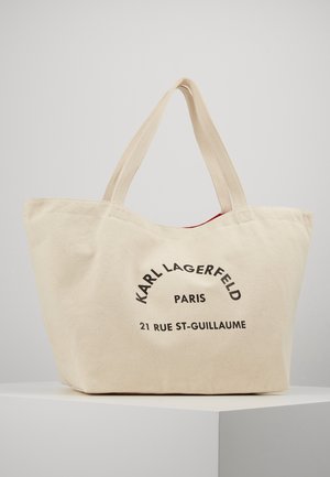 Beige lærredsnettaske med to håndtag, med sort trykt tekst "KARL LAGERFELD PARIS 21 RUE ST-GUILLAUME" på forsiden.
