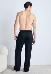 Black pajama pants with an elastic waistband and two back pockets, made from soft fabric, featuring a straight-leg design.