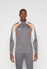 Šedá sportovní bunda se zipovým límcem, s oranžov�ými a bílými panely. Vyrobena z lehkého materiálu, má hladkou texturu a logo na hrudi.