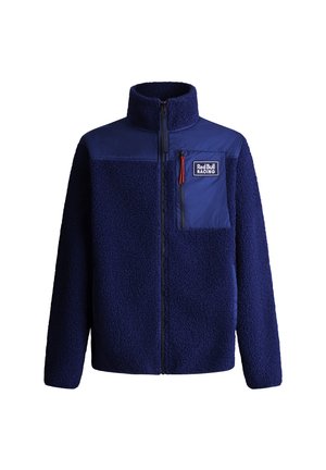 Chaqueta de forro polar azul marino con una sección superior de nylon liso, cuello alto, cremallera frontal y un bolsillo en el pecho con un pequeño tirador de cremallera roja.