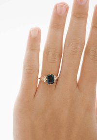 Anillo de zafiro engastado en oro rosa, con una piedra central de zafiro ovalada y dos pequeños acentos de diamante a cada lado.