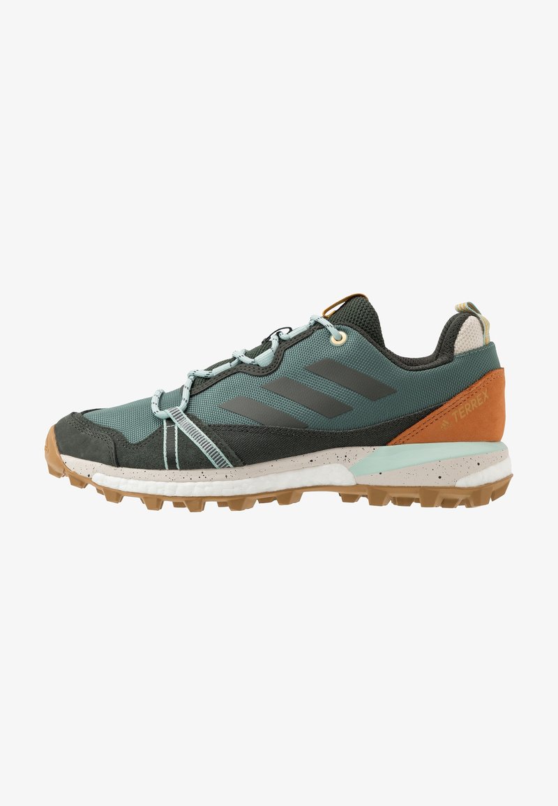 Chaussure de randonnée d'extérieur avec tissu turquoise, daim noir, patch marron au talon, lacets bleu clair, semelle robuste beige et logo trois bandes Adidas sur le côté.