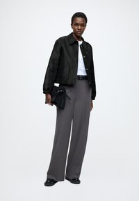 Μαύρο cropped σακάκι με υφή, λευκό πουκάμισο από κάτω, γκρι φαρδιά παντελόνια, μαύρη τσάντα χειρός και χοντρά μαύρα παπούτσια. Απλά χαρακτηριστικά σχεδίου.