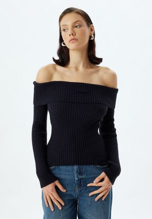 Top navy a spalle scoperte con maniche lunghe, caratterizzato da una silhouette aderente e tessuto testurizzato. Abbinato a jeans blu.