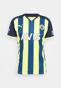 Sportowa koszulka Puma z pionowymi paskami w kolorze niebieskim i neonowożółtym, dekoltem w serek i fakturowanym wzorem. Z przodu znajduje się logo "AVIS" oraz herb drużyny.
