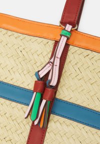 Spleciona torba ze słomy z czerwonymi i pomarańczowymi skórzanymi akcentami, z niebieskimi i zielonymi paskami oraz kolorowymi frędzlami ze skóry.