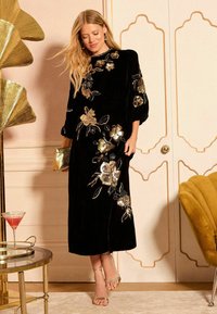 Rochie din catifea neagră cu broderie florală detaliată în aur și argint, cu tăietură medie și mâneci bufante. Purtați cu sandale cu bretele.