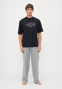 Camiseta negra de manga corta con gráfico en blanco que dice "VIBES", combinada con pantalones de algodón gris claro de corte relajado. Ambos son estilos de ropa casual para estar en casa.