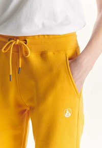 Geel joggerbroek van een zachte katoenmix, met een elastische tailleband, zijzakken en een wit logopatch. Glad textuur.