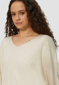 Hellbeige oversized Pullover mit V-Ausschnitt, weicher Textur und lockerer Passform, mit minimaler Nahtverarbeitung und entspannter Silhouette.