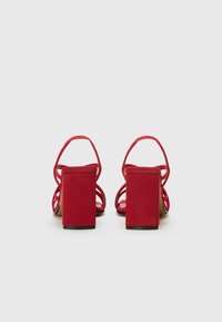 Rote High-Heelsandalen mit Blockabsatz, die dünne Riemen und ein offenes Rückendesign aufweisen. Hergestellt aus glattem Material mit matter Oberfläche.